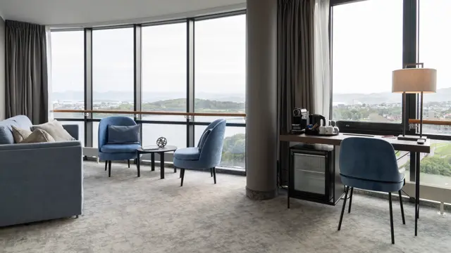Suite med skrivebord og lenestoler langs store viduer med utsikt.