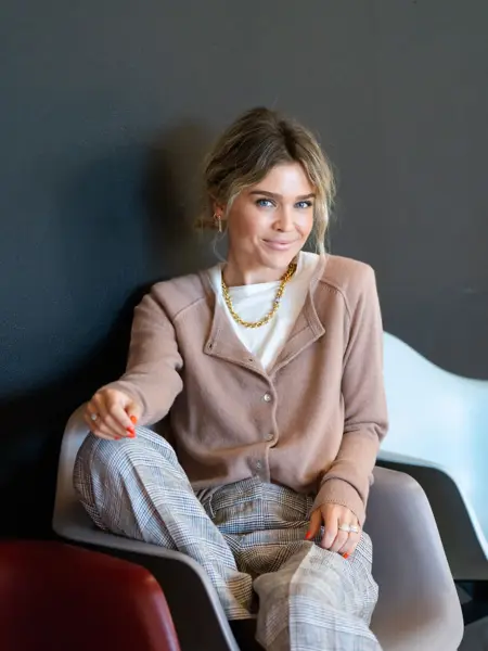 Ung kvinne som sitter i en stol mens hun poserer i trendy antrekk