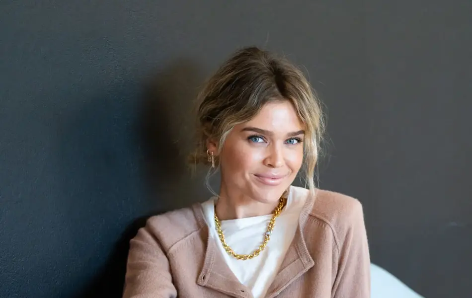 Ung kvinne som sitter i en stol mens hun poserer i trendy antrekk