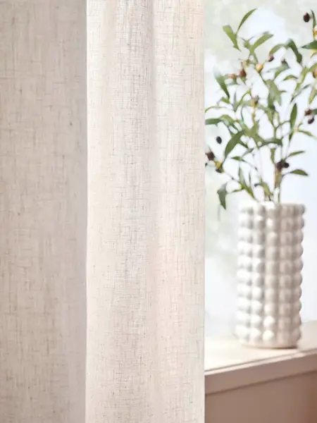 Gardiner foran et vindu med en hvit vase i vinduskarmen.
