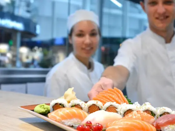 To sushi kokk som smiler og serverer sushi på benken