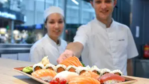 To sushi kokk som smiler og serverer sushi på benken