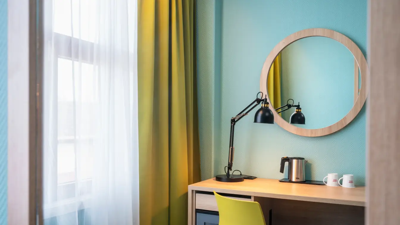 Turkis vegg, vindu, gule gardiner, skrivebord, gul stol, rundt veggspeil. 