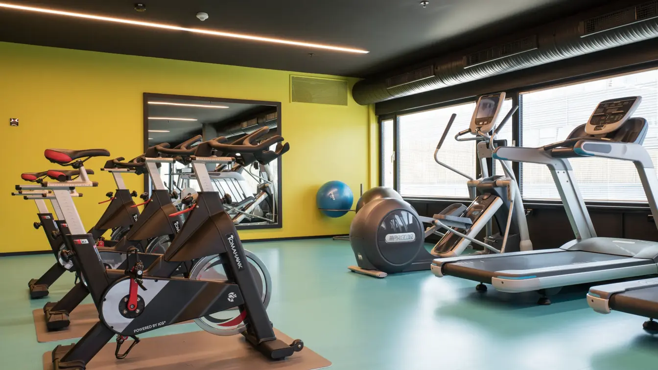 Treningsrom med spinningssykler og løpemaskin med gul og grønne farger på vegg og gulv på Thon Hotel Oslo Airport