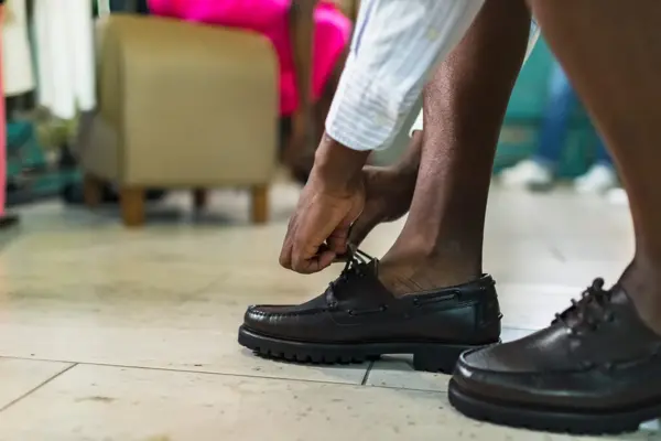 Nærbilde av mannehender som knytter svarte loafers