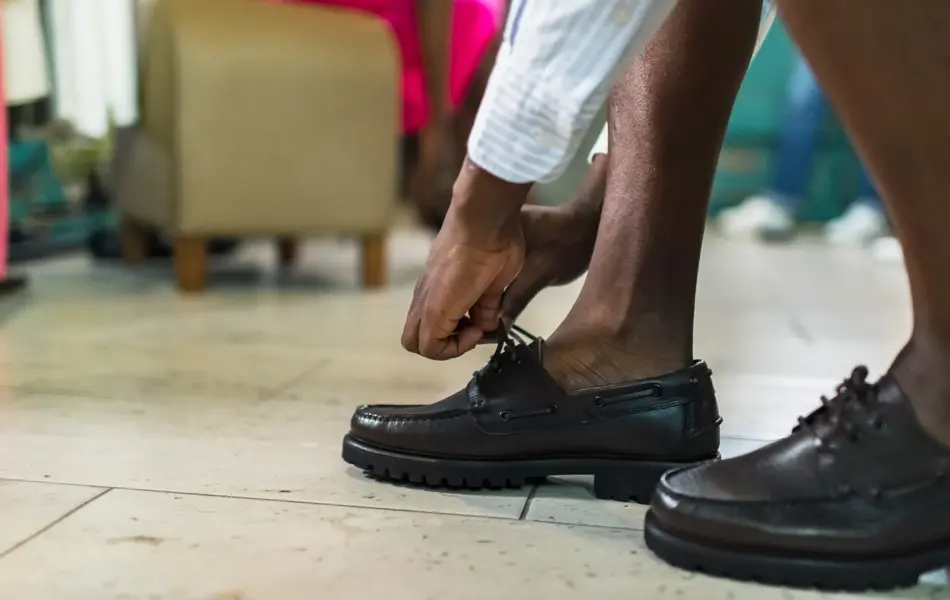 Nærbilde av mannehender som knytter svarte loafers