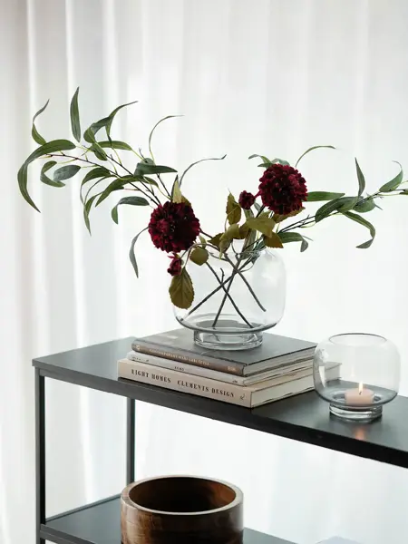 Konsollbord med trekrukk, telysholder og en vase med blomster på tre bøker.