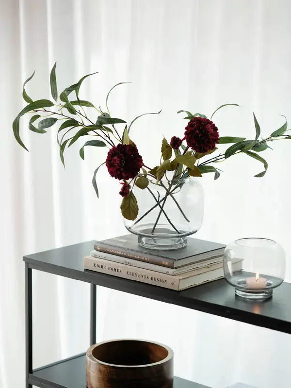Konsollbord med trekrukk, telysholder og en vase med blomster på tre bøker.