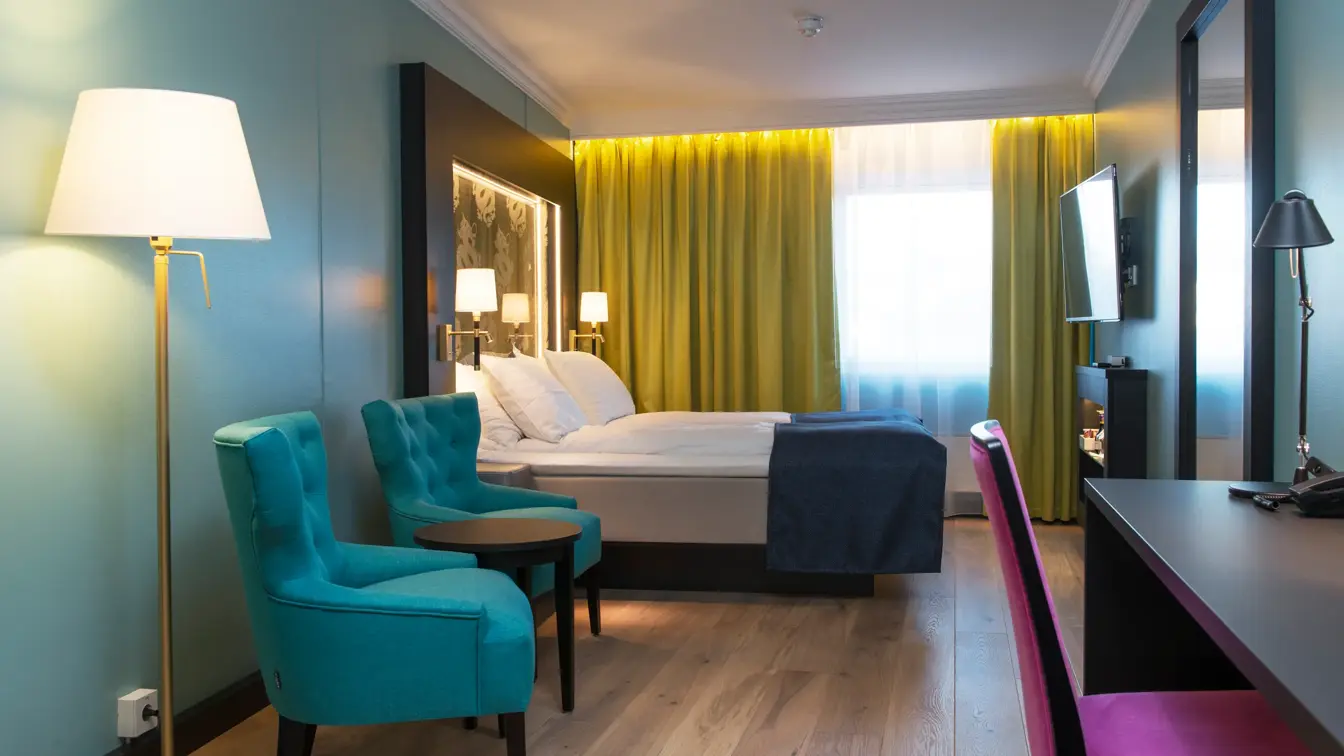 Dobbeltseng blå lenestol, gule gardiner, skrivepult med lilla stol og dragemlnster på seng på Thon hotel Terminus i Oslo sentrum nær Jernbanetorget