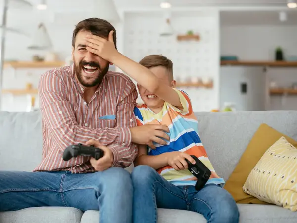 Gutt holder hånden foran øynene til mann mens de spiller tv-spill. Foto til artikkel om opplevelsesgaver til farsdag