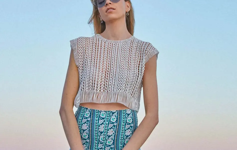 Dame med mønstrete bukse og heklet sølvtopp ser i kamera 