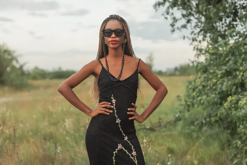 Dame med sort kjole med litt blonder poserer foran gresslette og trær