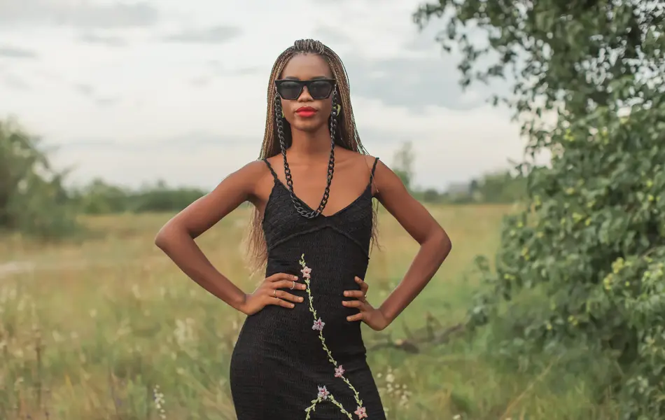 Dame med sort kjole med litt blonder poserer foran gresslette og trær