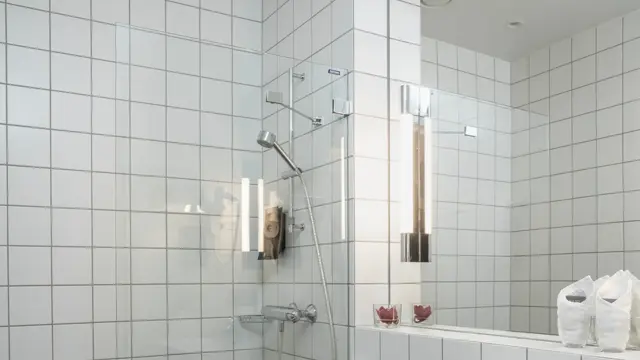 Vegger med hvite fliser, dusjhjørne med glassvegg, speil over hvit servant og gulv med grå fliser. I standard baderom på Thon Hotel Høyers i Skien.