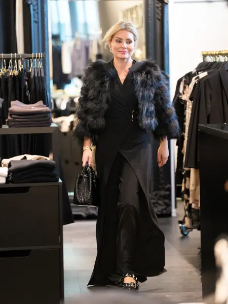 Dame med kort fuskepels jakke, sort lang kjole og sorte flate sko.