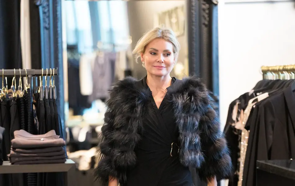 Dame med kort fuskepels jakke, sort lang kjole og sorte flate sko.