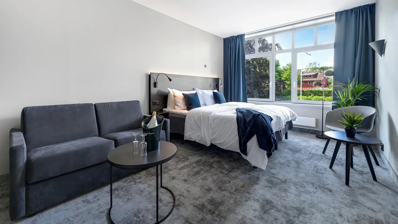 Dobbeltseng, grå sofa, salongbord, lenestol, salongbord, vindu, blå gardiner 