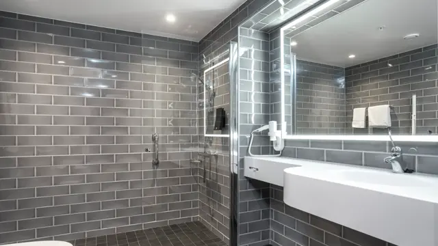 Vegger og gulv med grå fliser, dusjhjørne med glassvegg, speil med LED lys rundt og hvit servant. I superior baderom på Thon Hotel Høyers i Skien.