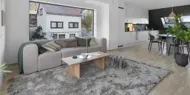 Bilde av stue med sofa, bord, stort teppe og stort vindu fra boligprosjektet Saras Hage i Tromsø