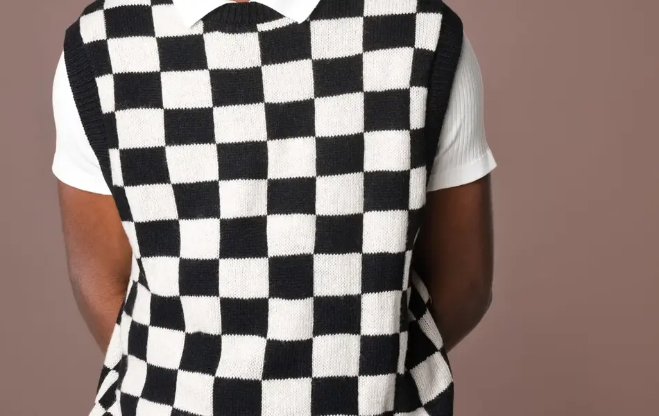 Mann i hvit og sortrutete vest, hvit t-skjorte og oransje teddybøttehatt smiler til kamera 