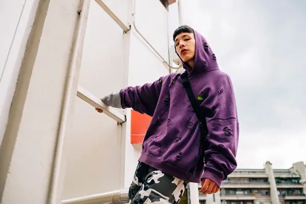 Kul ung mann iført hetteskjorte stående på metallisk stige mot himmelen