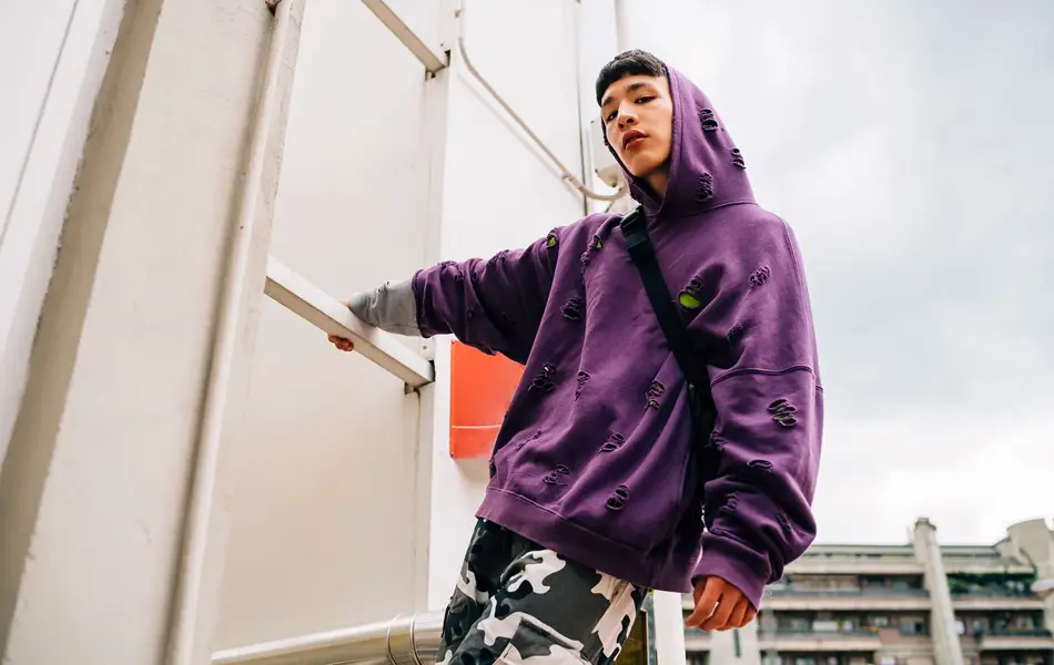 Kul ung mann iført hetteskjorte stående på metallisk stige mot himmelen