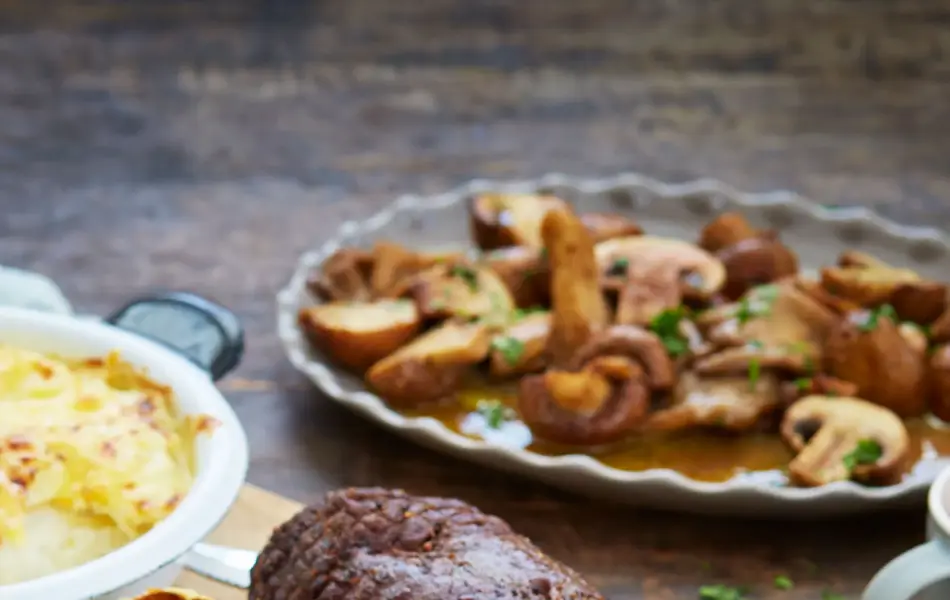 Fjøl med oppskåret hjortestek med fløtegratinerte poteter og tilbehør ved siden av