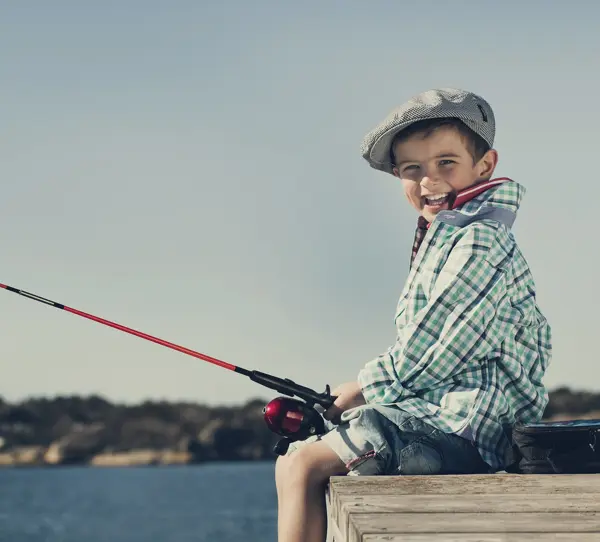 gutt som sitter på brygga og fisker