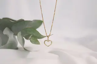 Et gullsmykke med hjerteanheng henger foran en plante.