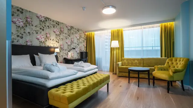 Blomstrete tapetvegg, gule gardiner, gul sofa, gul stol, parkettgulv, dobbeltseng, blå vegger. 