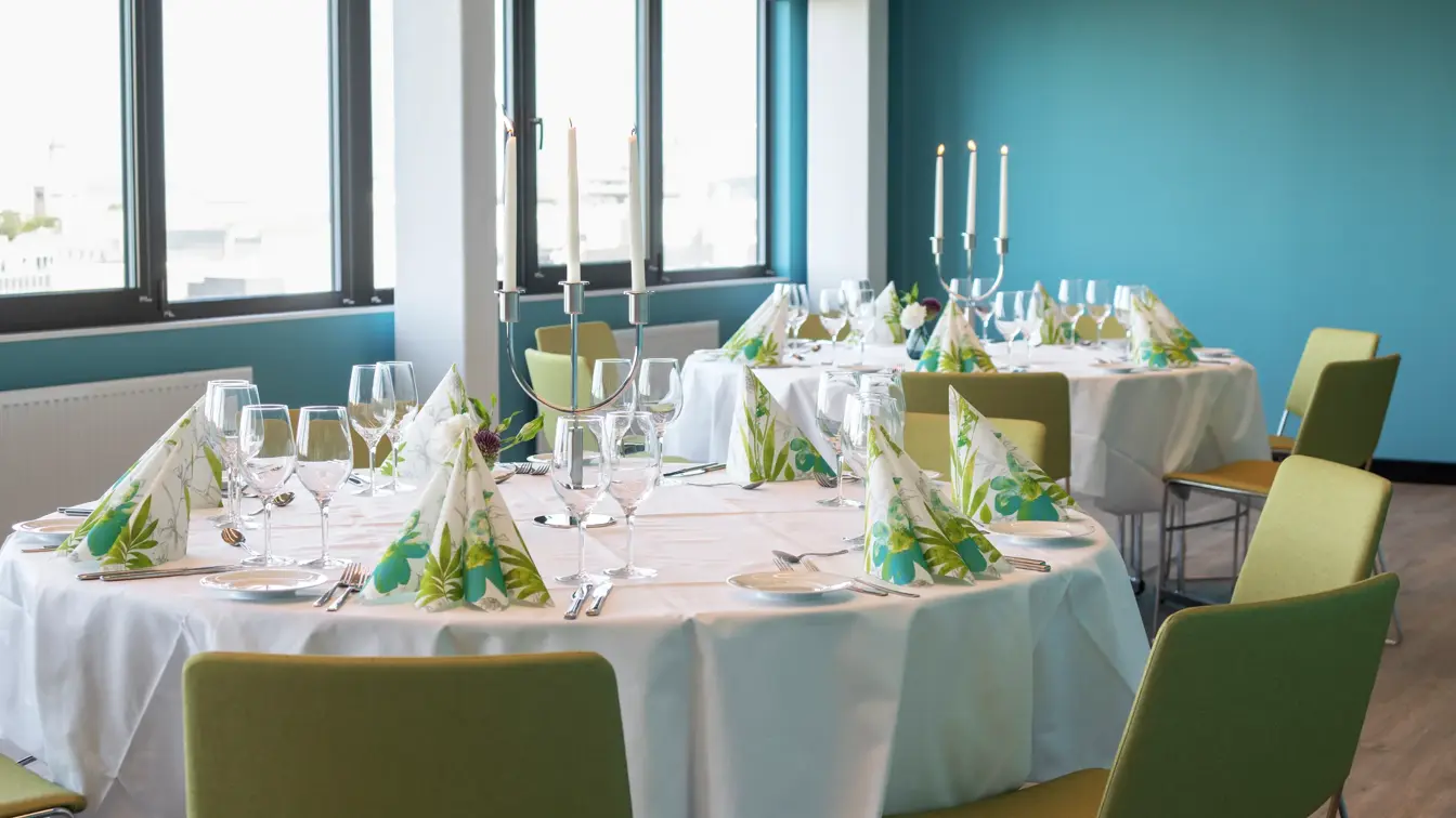 Dekkete bord med hvite duker og fargerike servietter i selskapslokale Lysefjord, med store vinduer, på Thon Hotel Maritim