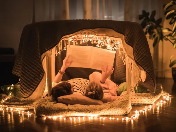 Mother and daughter lying inside of a tent at home and enjoying in book reading.