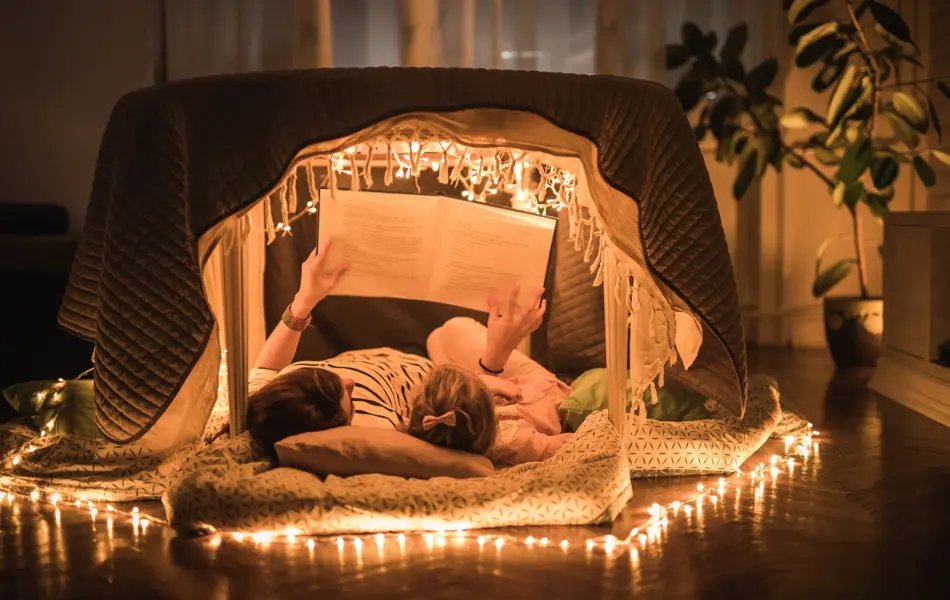 Mother and daughter lying inside of a tent at home and enjoying in book reading.