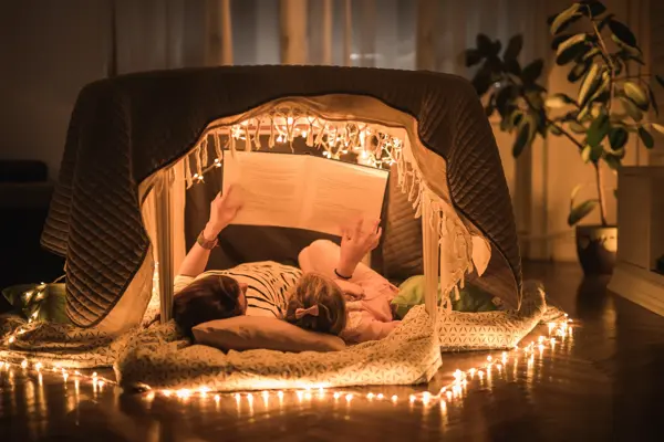 Mother and daughter lying inside of a tent at home and enjoying in book reading.