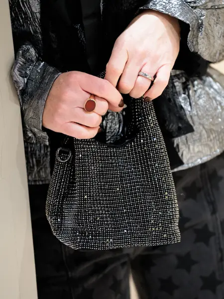 Hender med ringer, holder en liten paljettveske, sort bukse, sølv bluse.