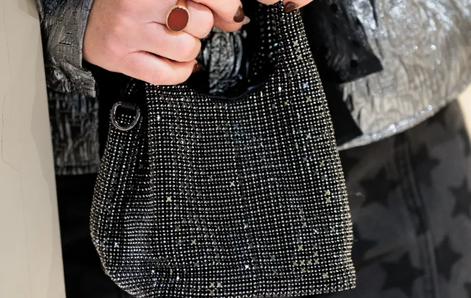 Hender med ringer, holder en liten paljettveske, sort bukse, sølv bluse.