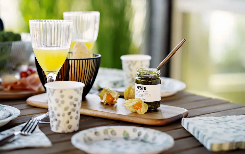 Skål med grønnkål og et dekket bord med mat og papptallerken.