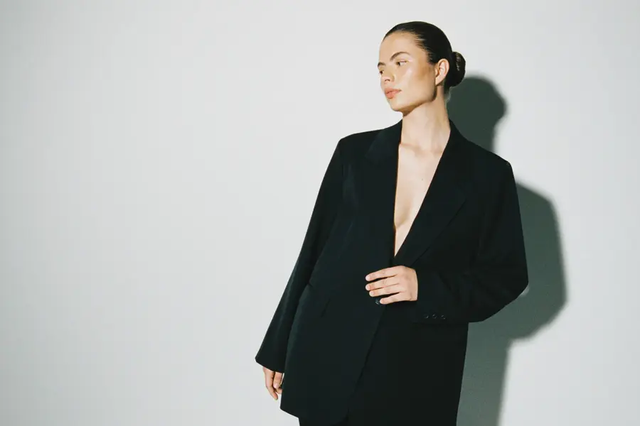 En kvinne i en sort dress foran en grå vegg