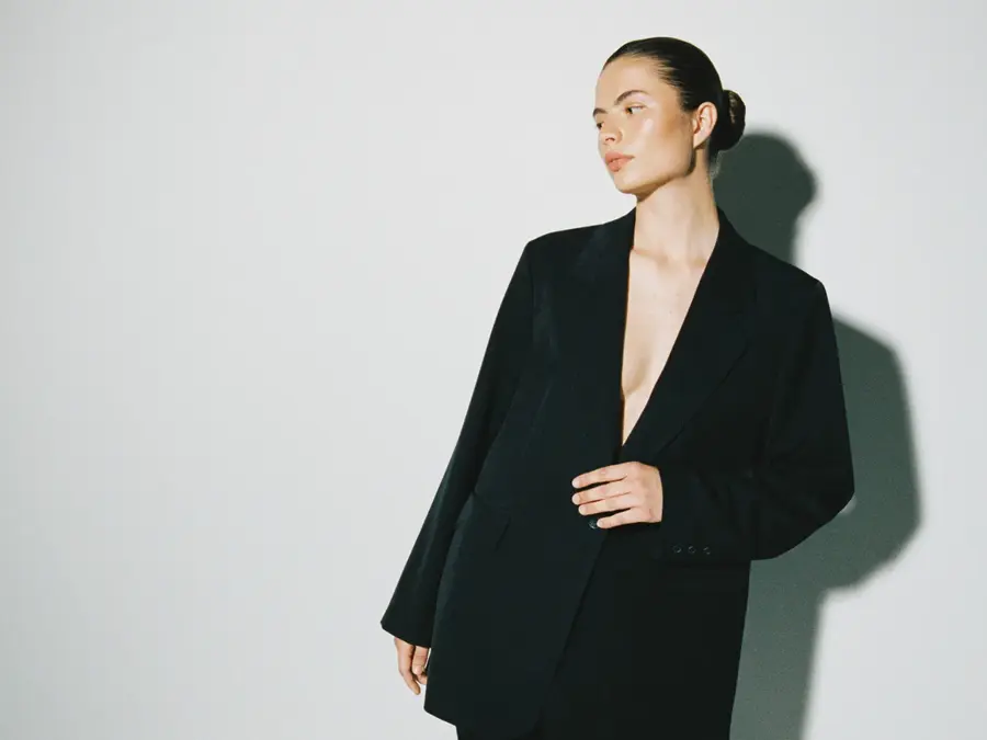 En kvinne i en sort dress foran en grå vegg