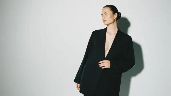 En kvinne i en sort dress foran en grå vegg