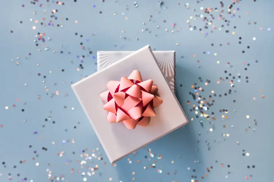 White silver gift boxes with pink bow on blue background in trendy flat lay composition with shiny glitters.