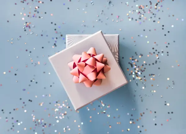 White silver gift boxes with pink bow on blue background in trendy flat lay composition with shiny glitters.