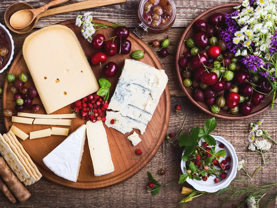 Cheese platter with fresh colorful summer berries and wild flowers, rural savory dessert background viewed from above