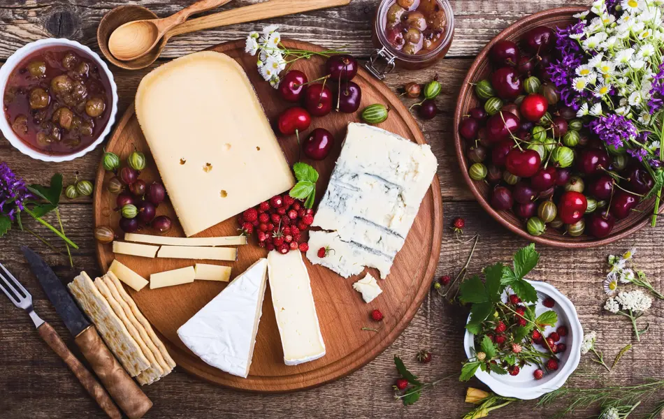 Cheese platter with fresh colorful summer berries and wild flowers, rural savory dessert background viewed from above