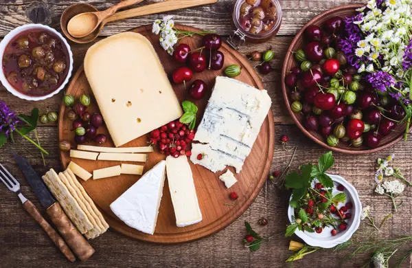 Cheese platter with fresh colorful summer berries and wild flowers, rural savory dessert background viewed from above