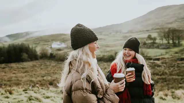 To jenter i vinterjakker går og prater med kaffe i hånda 