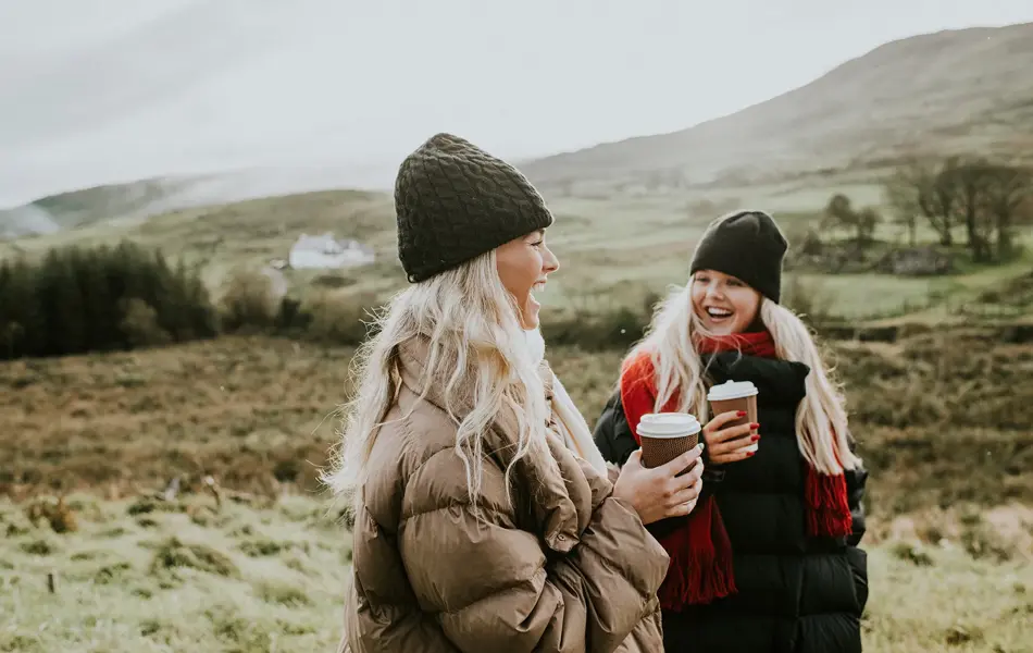To jenter i vinterjakker går og prater med kaffe i hånda 