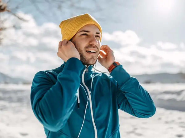Mann i vinterlandskap med gul lue som fester øreplugger