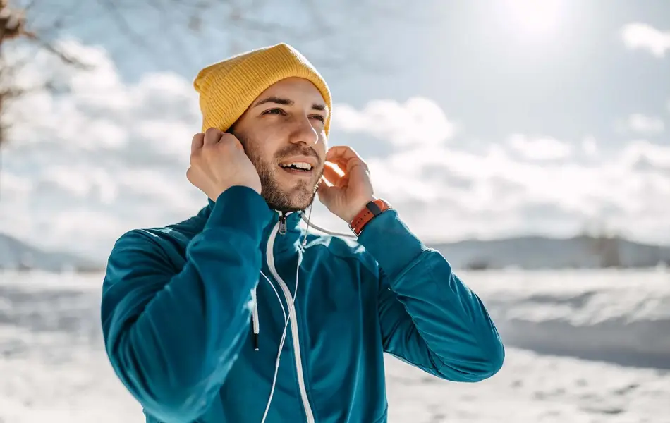 Mann i vinterlandskap med gul lue som fester øreplugger