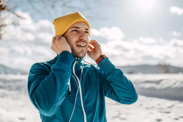 Mann i vinterlandskap med gul lue som fester øreplugger